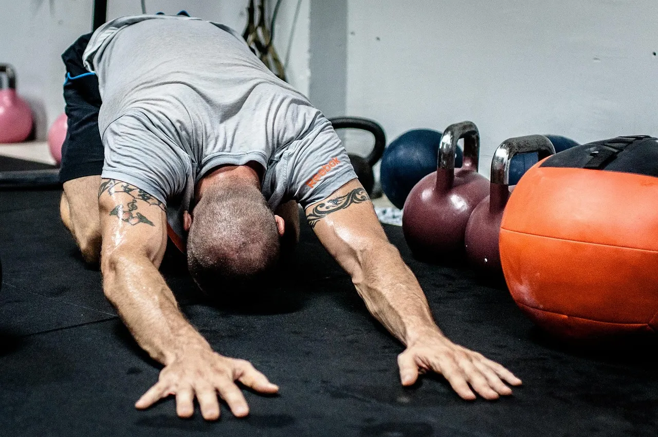 A man performing a deep stretch on a gym floor beside kettlebells, reflecting the active recovery habits that complement passive tools like compression