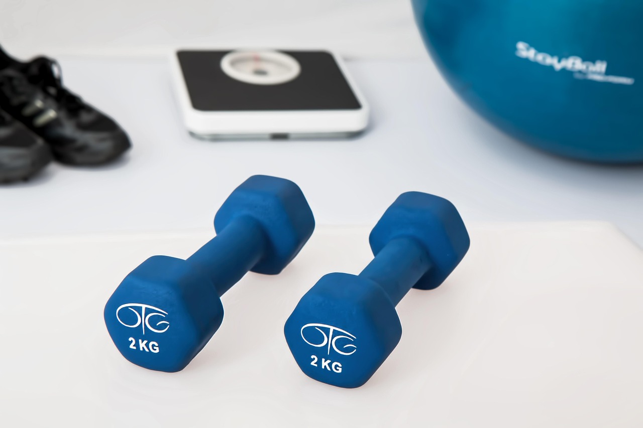 Dumbbells, a bathroom scale, and an exercise ball laid out for a strength workout, representing the training loads creatine research examines