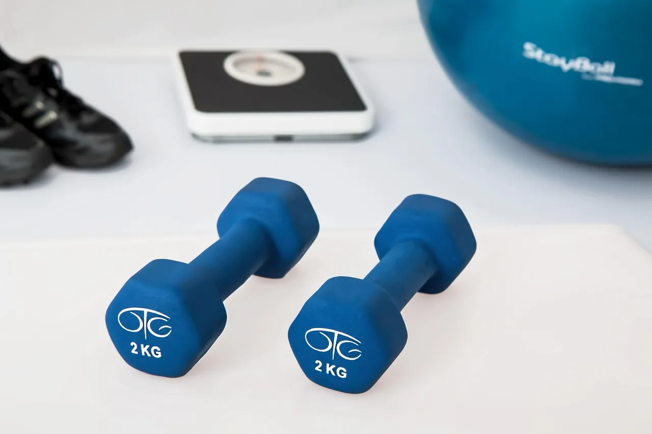 Dumbbells, a bathroom scale, and an exercise ball laid out for a strength workout, representing the training loads creatine research examines
