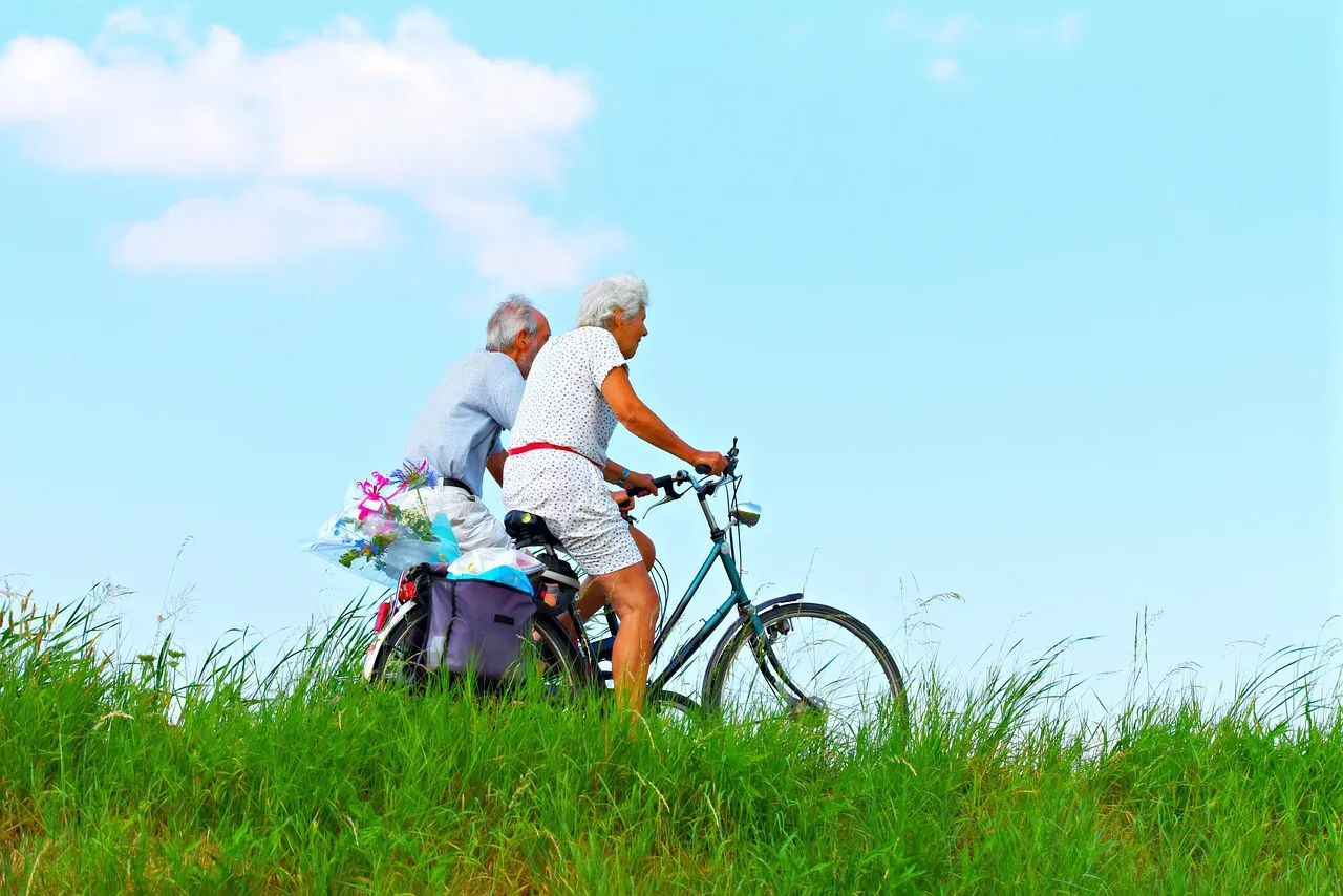 An older couple cycling together on a sunny road, an example of the aerobic activity studied in frailty-prevention exercise trials
